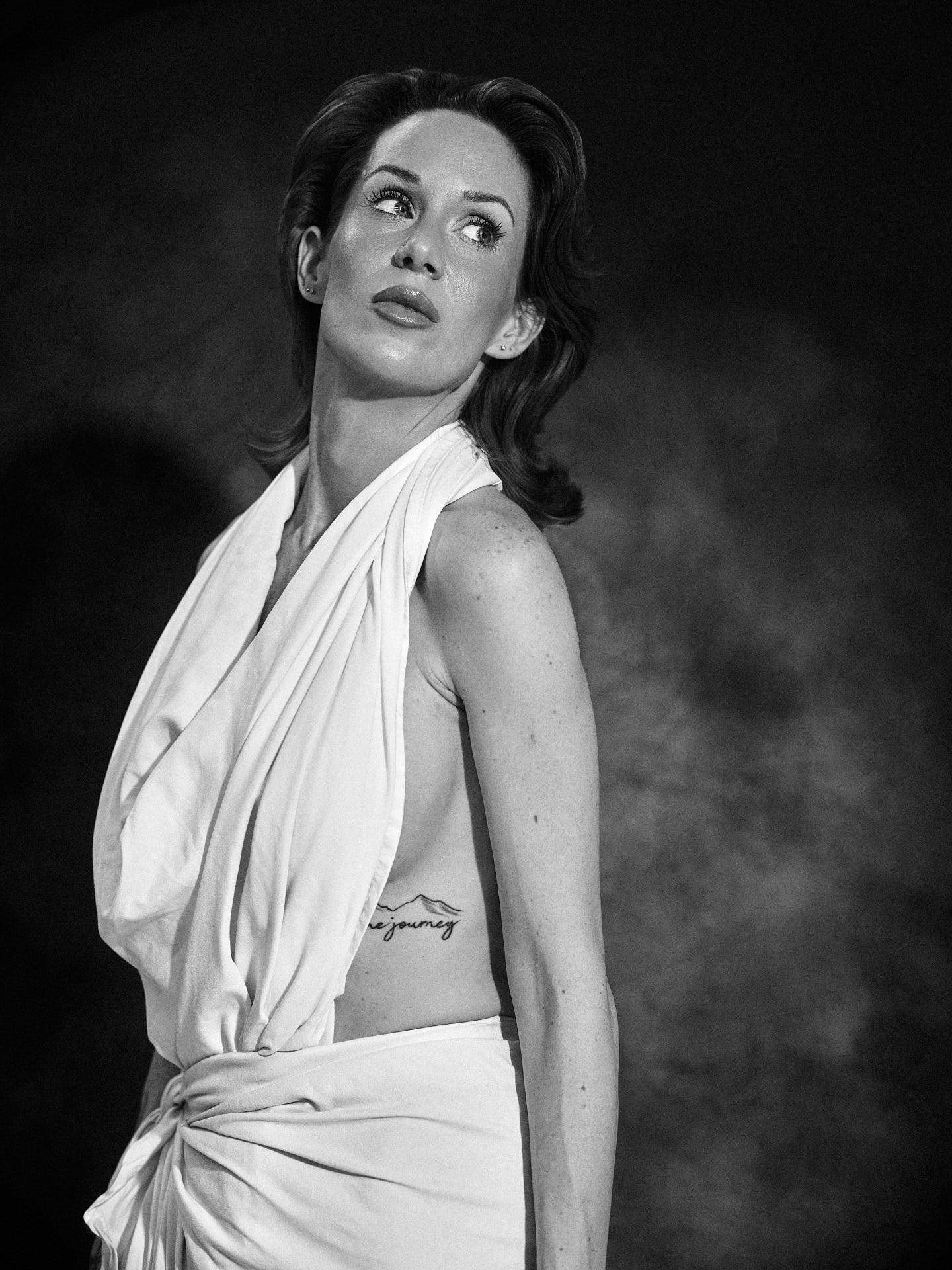 Black and white portrait of a woman in draped white fabric against a dark backdrop