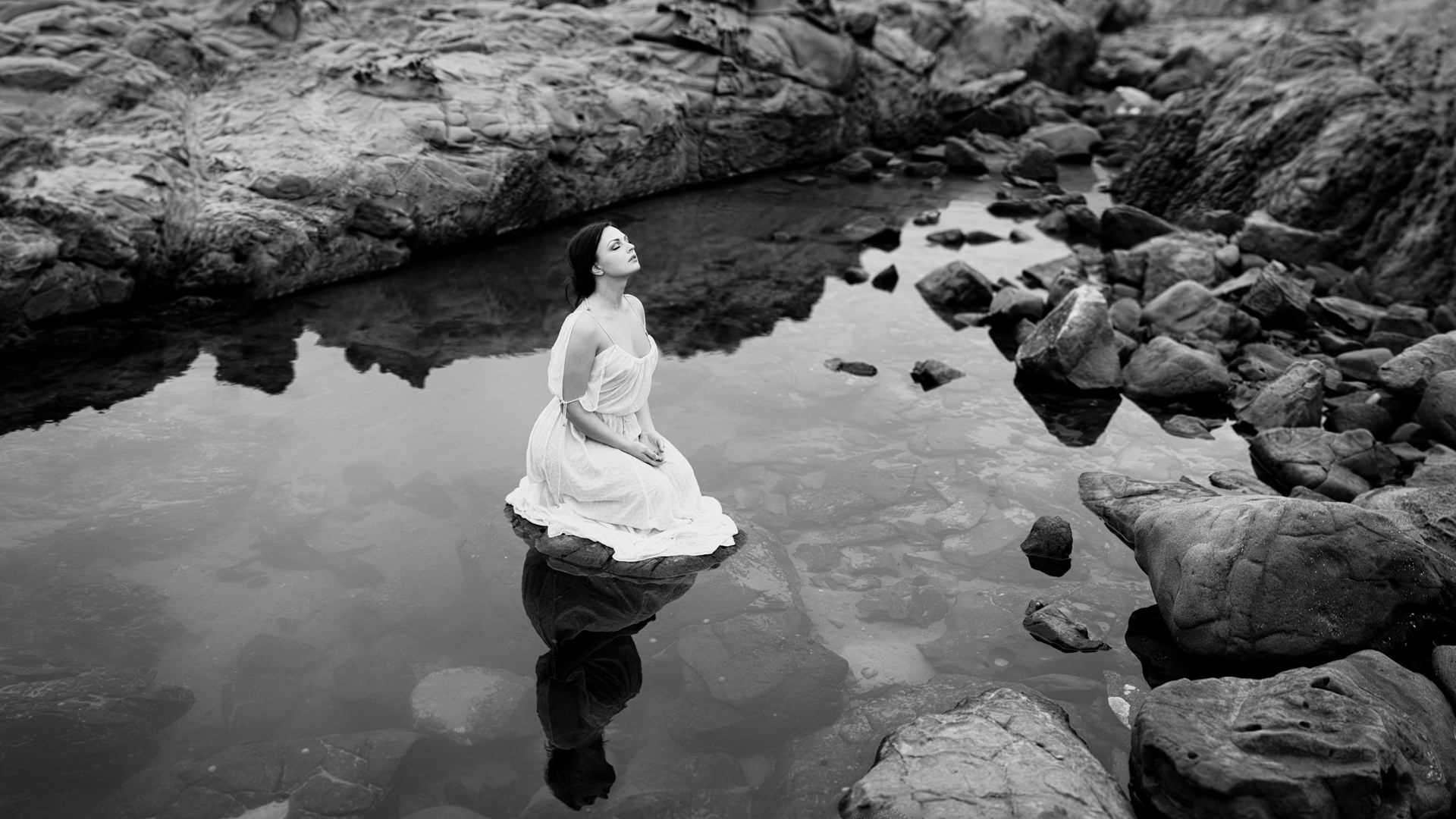 Black and white portrait seated in water among rocks